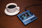 1010music Bluebox digital mixer with colorful knobs and interface, shown in a lifestyle setting with cables and music gear.