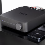 WiiM AMP music streamer device with sleek black design, front display, and connectivity ports for high-quality audio streaming.