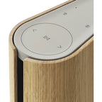Bang & Olufsen Beosound Emerge wireless speaker in gold tone with sleek, modern design and fabric cover.