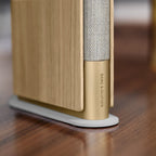 Bang & Olufsen Beosound Emerge wireless speaker in gold tone, featuring a sleek, modern design with fabric grille and smooth finish.