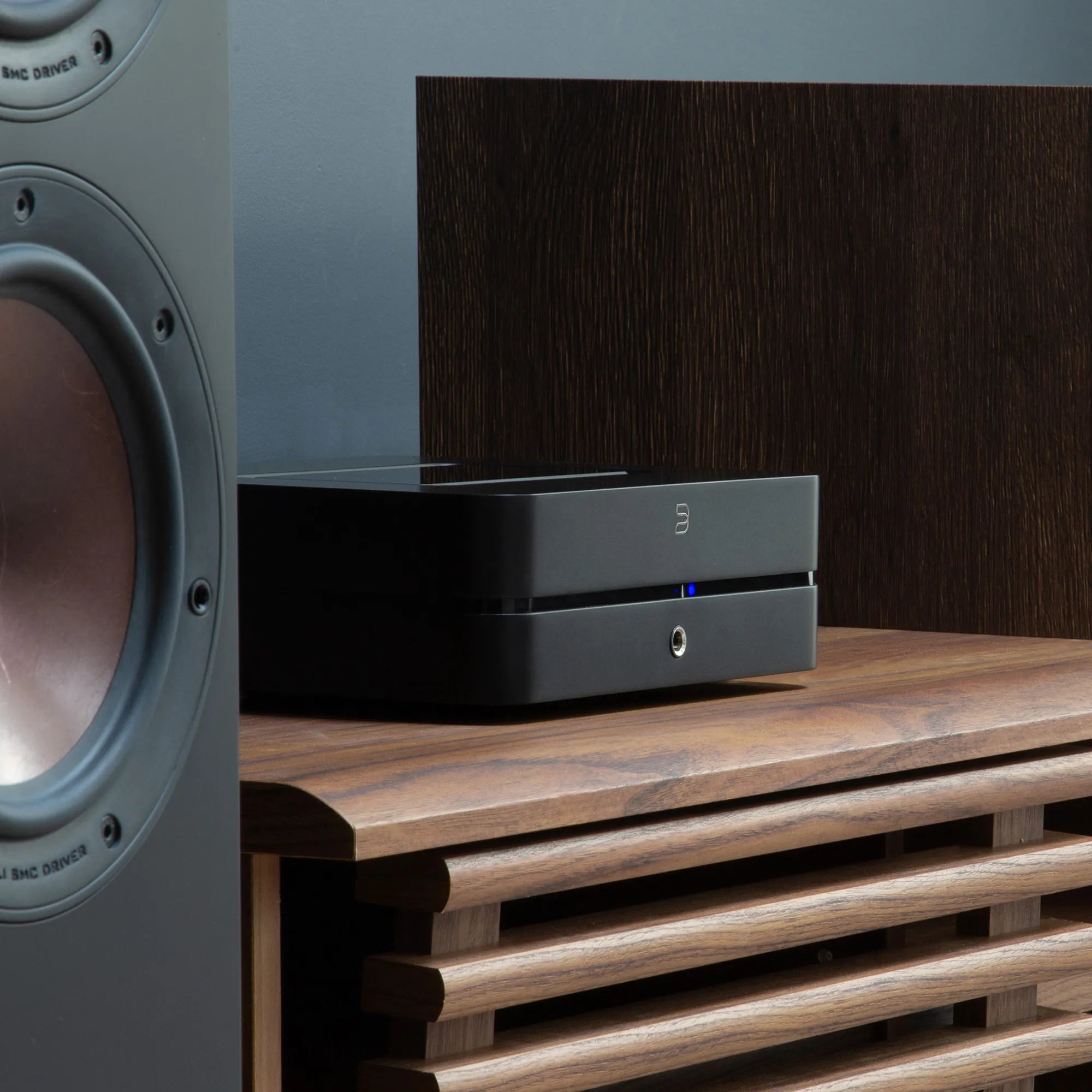 Bluesound Powernode 2025 music streamer in black, shown with DALI Opticon 6 MK2 speakers, close-up low right angle.
