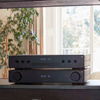 Arcam A5+ stereo amplifier shown in a lifestyle setting, featuring sleek design and controls for high-quality audio performance.