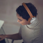 Bang & Olufsen Beoplay HX wireless headphones in timber finish, shown worn in a lifestyle setting with sleek design elements.