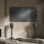 KEF LS Luxe in Eclipse Black on floor stands beside a wall-mounted TV in a plaster living room