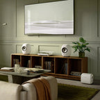 KEF LS Luxe in Mineral White on a walnut credenza with a wall-mounted TV and KEF subwoofer