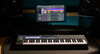 Novation FLkey 61 MIDI keyboard with illuminated pads and control knobs, shown in a music studio setup.