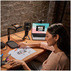 Rode DS3 black desktop studio arm on a wooden desk beside a laptop during a remote work session