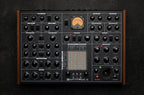 Erica Synths SYNTRX II desktop synthesizer with knobs, buttons, and OLED display on a black surface.